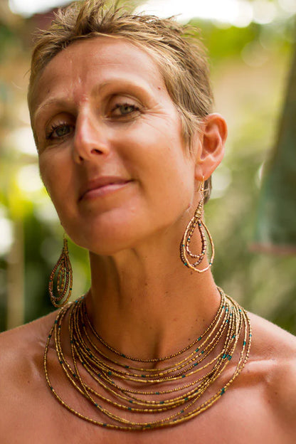 Model wearing the Grecian Goddess Earrings and Necklace, handmade in India. The earrings feature a combination of bronze, teal, and chocolate brown beads, while the necklace boasts a matching pendant on a delicate chain. The model is shown with a confident expression, highlighting the timeless beauty of the jewelry. The earrings take center stage, while the necklace complements the look with its elegant simplicity.