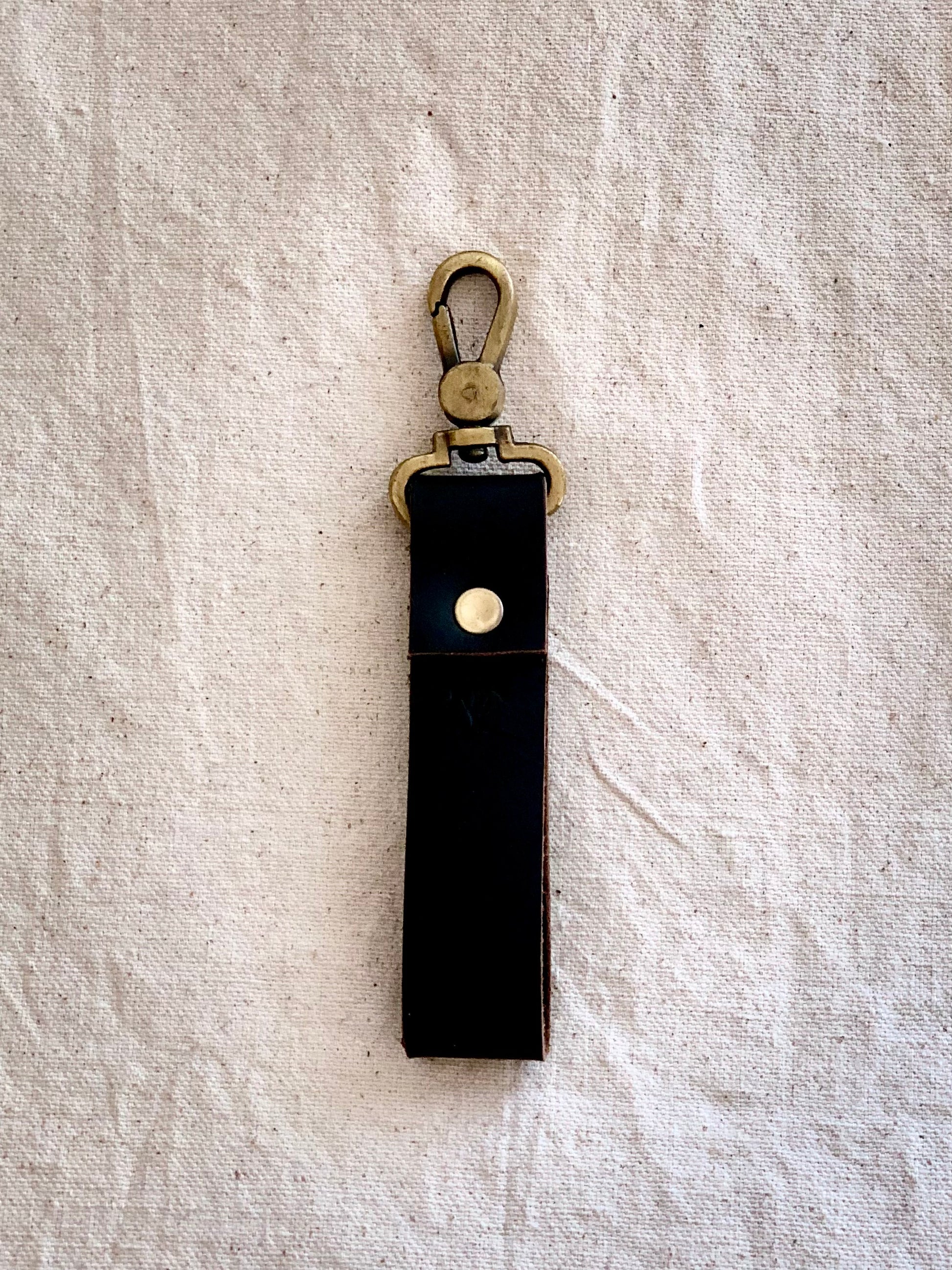 Photo of the Leather Key Strap, showcasing the premium quality leather and brass clasp that holds your keys. The loop at the other end makes it easy to attach to your belt, bag, or for holding, while the simple yet elegant design complements any style. The photo shows the key strap attached to a model's bag, with a focus on the intricate details and the high-quality materials used in crafting the strap.