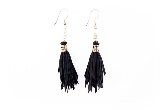 Photo of the Black Leather Tassel Earrings, showcasing the soft black suede and delicate tassels handcrafted by skilled artisans. The earrings are lightweight and easy to wear, making them perfect for everyday wear or a night out. The photo shows the earrings worn by a model, with a focus on the intricate details and the high-quality materials used in crafting the earrings. Add some playful charm to your style with our Black Leather Tassel Earrings.