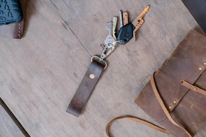 Photo of the Leather Key Strap, showcasing the premium quality leather and brass clasp that holds your keys. The loop at the other end makes it easy to attach to your belt, bag, or for holding, while the simple yet elegant design complements any style. The photo shows the key strap attached to a model's bag, with a focus on the intricate details and the high-quality materials used in crafting the strap.